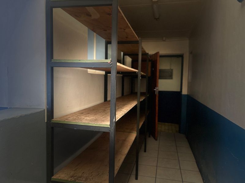 A functional utility or storage space featuring tiled flooring, built-in metal shelving units, and basic overhead lighting.