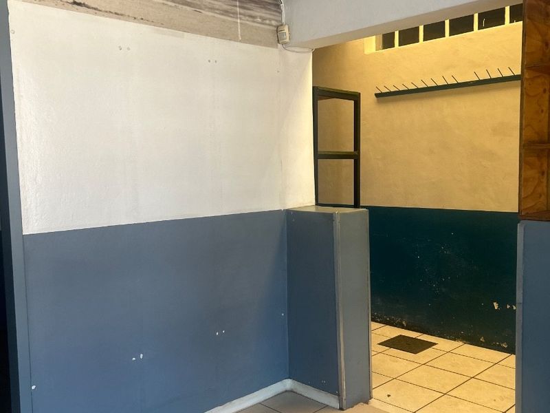 An empty office space featuring tiled flooring, built-in wall shelving, and wall-mounted hooks, requiring cosmetic updates to the wall finishes.