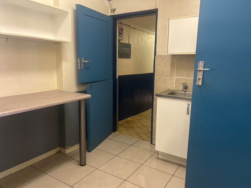 A functional scullery or utility area featuring a stainless steel sink, built-in cabinetry, laminate countertop, and tiled flooring with access to an adjacent corridor.