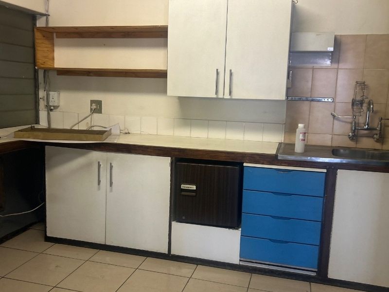 A functional kitchenette area featuring built-in cabinetry, laminate countertops, a stainless steel sink, and tiled flooring, suitable for office staff use.