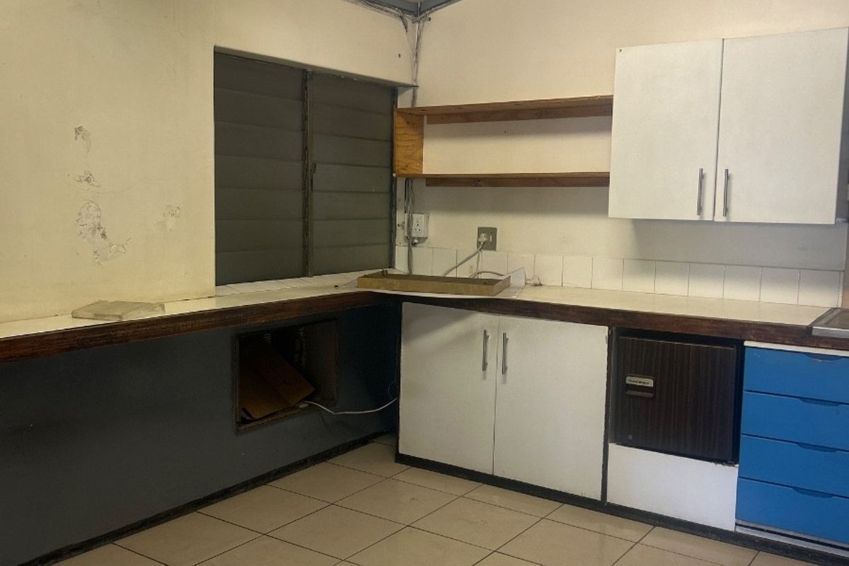 A dated kitchen area featuring tiled floors, built-in cabinetry, and a louvered window, currently in need of cosmetic renovation and repairs.