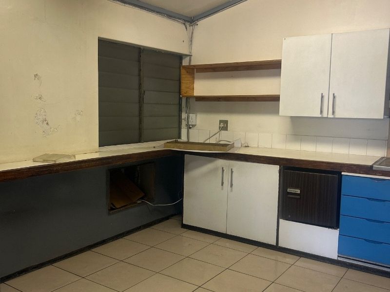 A dated kitchen area featuring tiled floors, built-in cabinetry, and a louvered window, currently in need of cosmetic renovation and repairs.