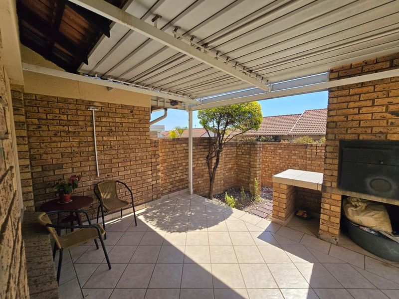 Covered outdoor patio featuring brick masonry walls, tiled flooring, and a built-in braai area, perfect for outdoor entertaining.