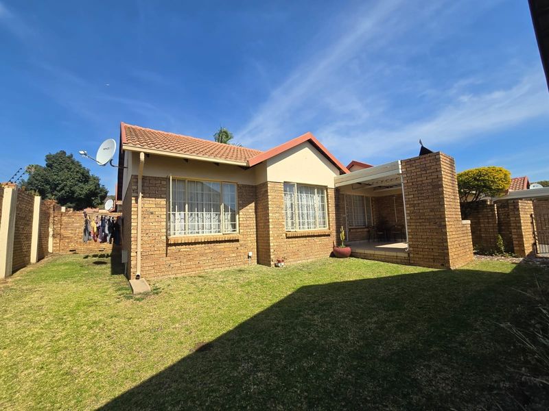 Rear view of a face brick townhouse featuring a covered patio, private garden, and secure perimeter fencing.