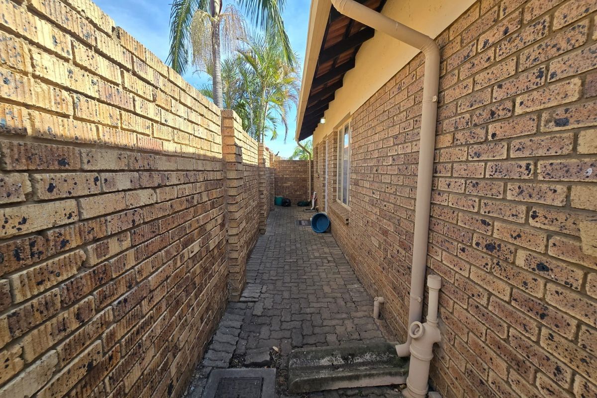 A narrow side passage of the townhouse featuring face brick walls and paved flooring with integrated drainage infrastructure.