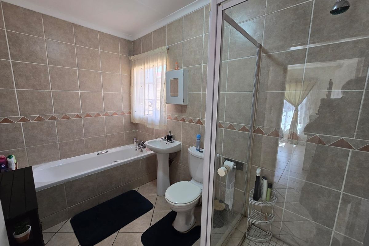 A functional bathroom featuring a bathtub, pedestal basin, toilet, and a separate glass-enclosed shower with neutral wall and floor tiling.