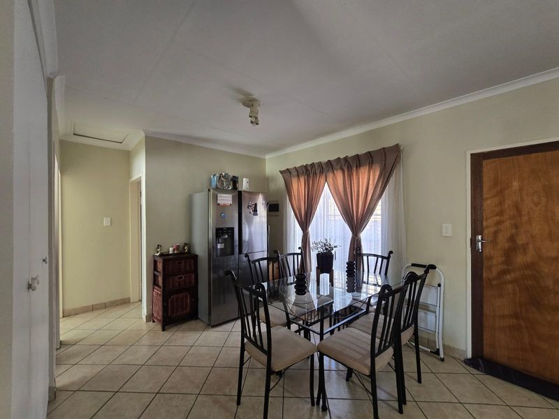 A functional dining area featuring neutral tiled flooring, coved ceilings, and a solid timber door, providing a practical space for family meals.