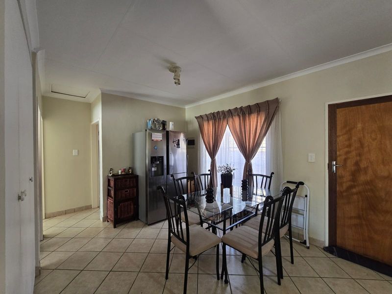 A functional dining area featuring neutral tiled flooring, standard ceiling finishes, and a solid wood door leading to adjacent spaces.