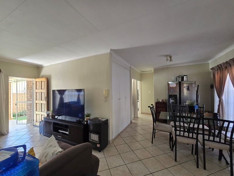 Open-plan living and dining area featuring tiled flooring, built-in storage cupboards, and direct access to an outdoor patio through a security gate.