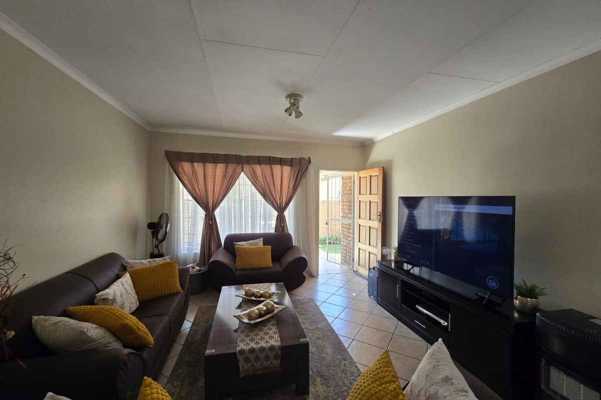 A comfortable living room featuring tiled flooring, ceiling coving, and direct access to the exterior through a security gate.