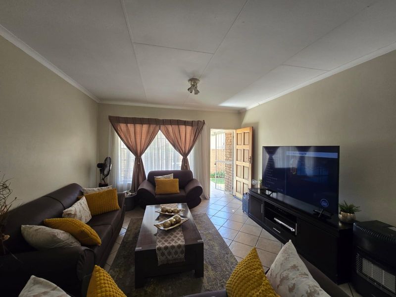 A comfortable living room featuring tiled flooring, ceiling coving, and direct access to the exterior through a security gate.