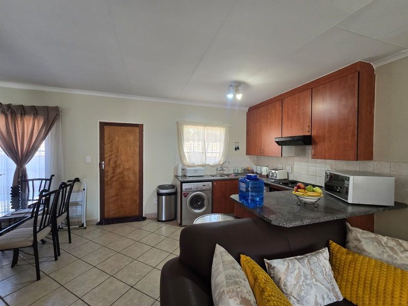 Open-plan kitchen and dining area featuring wooden cabinetry, granite countertops, tiled flooring, and a functional layout with integrated laundry plumbing.