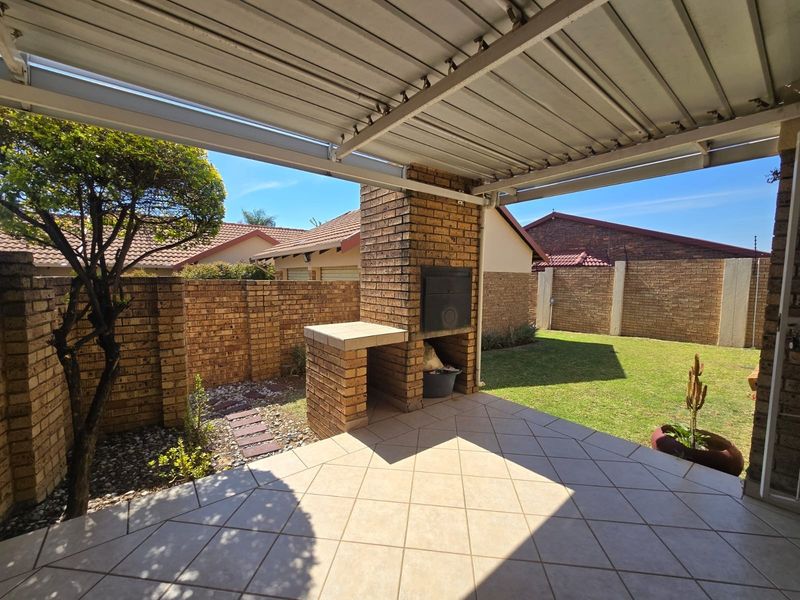 A covered outdoor patio featuring a built-in brick braai, tiled flooring, and direct access to a private garden area.