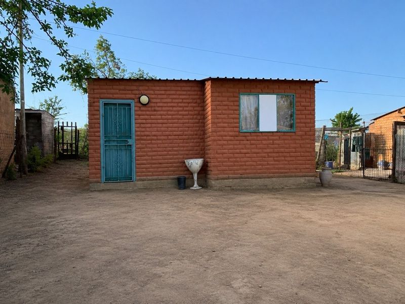A detached single-story structure featuring exposed brick walls, a metal security door, and a corrugated metal roof, situated on an unpaved lot.