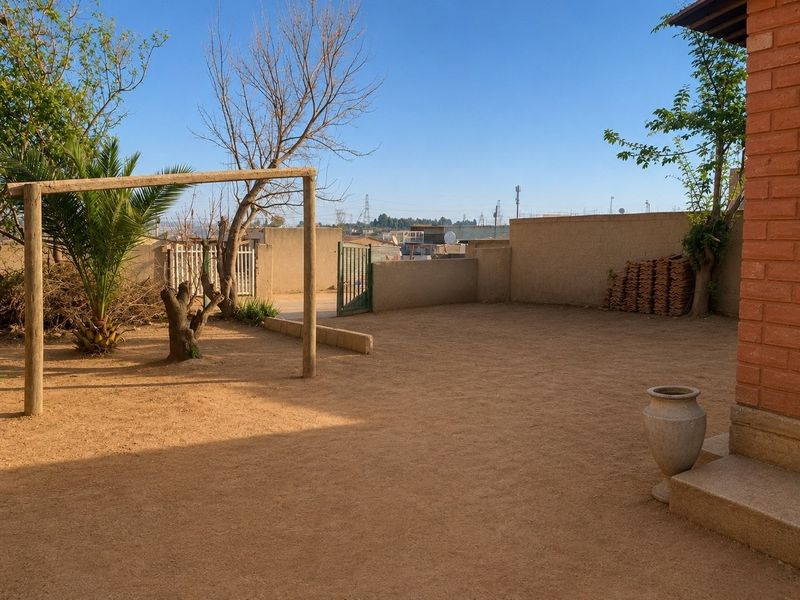 A spacious rear yard featuring a perimeter wall, metal gate, and brick exterior wall, offering a blank canvas for landscaping or outdoor improvements.