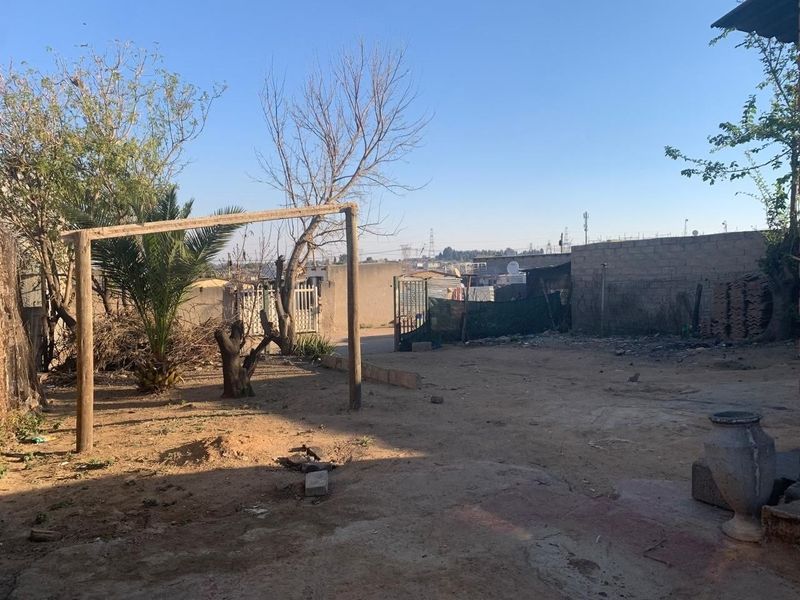 A spacious rear yard area featuring a perimeter wall, metal gate access, and an unpaved ground surface with potential for landscaping development.