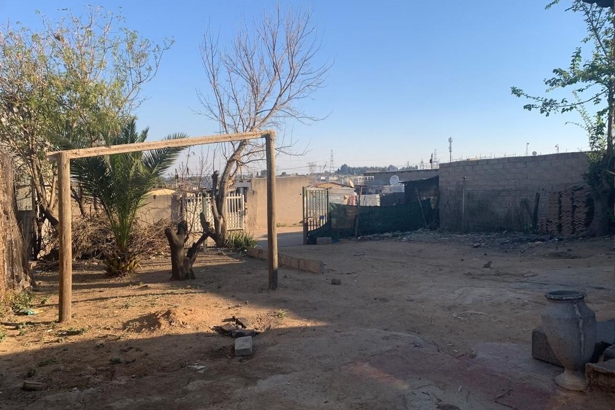 A spacious rear yard area featuring a perimeter wall, metal gate access, and an unpaved ground surface with potential for landscaping development.