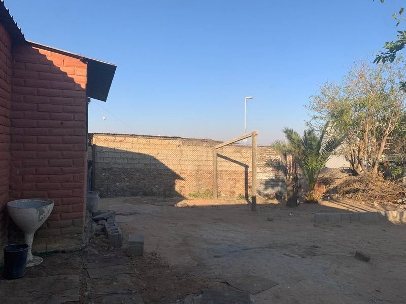 A rear exterior area featuring a brick building facade, a perimeter fence, and an unpaved yard space.