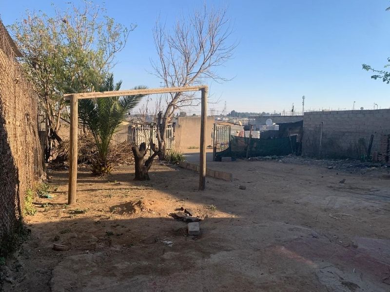 A spacious, unpaved rear yard area enclosed by perimeter walls and fencing, offering potential for landscaping or outdoor development.