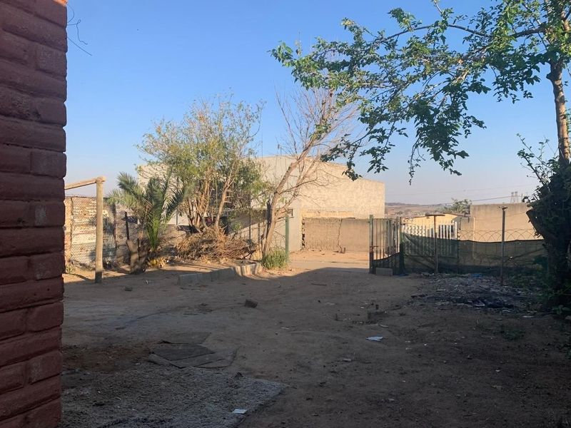 A spacious rear yard area featuring perimeter walling, metal gate access, and unpaved ground, offering potential for landscaping or outdoor development.
