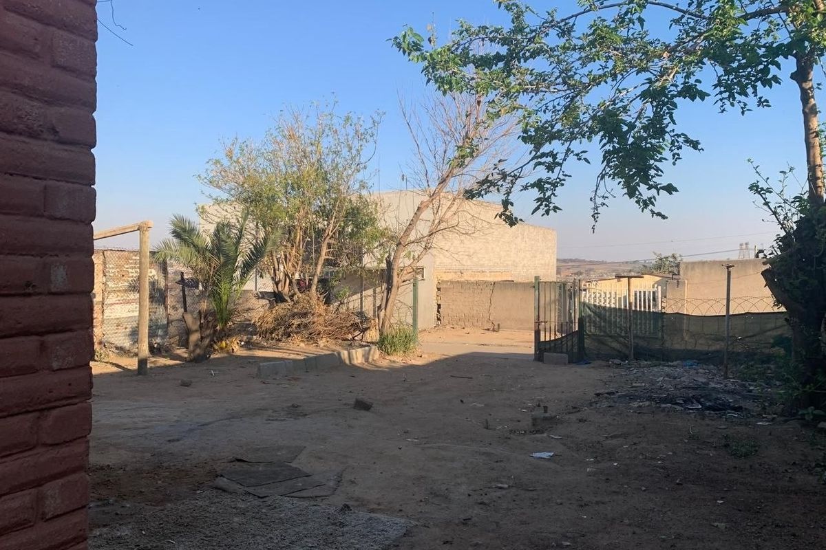 A spacious rear yard area featuring perimeter walling, metal gate access, and unpaved ground, offering potential for landscaping or outdoor development.