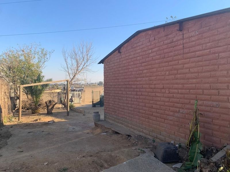 A view of the rear exterior of the property featuring an exposed brick wall and an unpaved yard area.