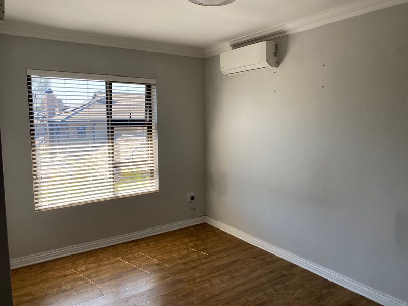 An empty bedroom featuring laminate flooring, venetian blinds, and a wall-mounted air conditioning unit.
