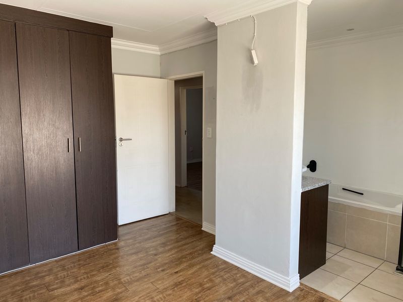 A bedroom featuring built-in cupboards, laminate flooring, and an open-plan en-suite bathroom area with a built-in bathtub and vanity.