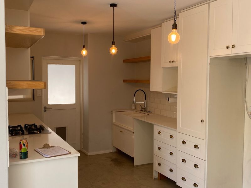 A modern, clean kitchen featuring white cabinetry, quartz countertops, an apron sink, gas hob, and stylish pendant lighting.