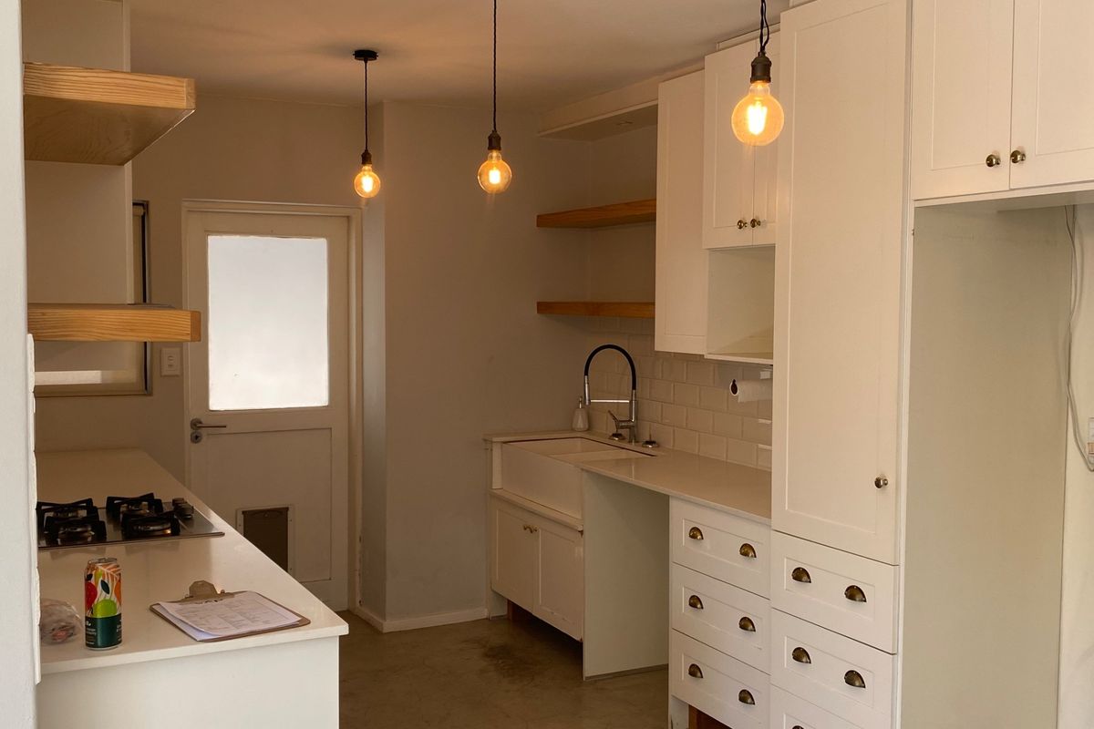 A modern, clean kitchen featuring white cabinetry, quartz countertops, an apron sink, gas hob, and stylish pendant lighting.