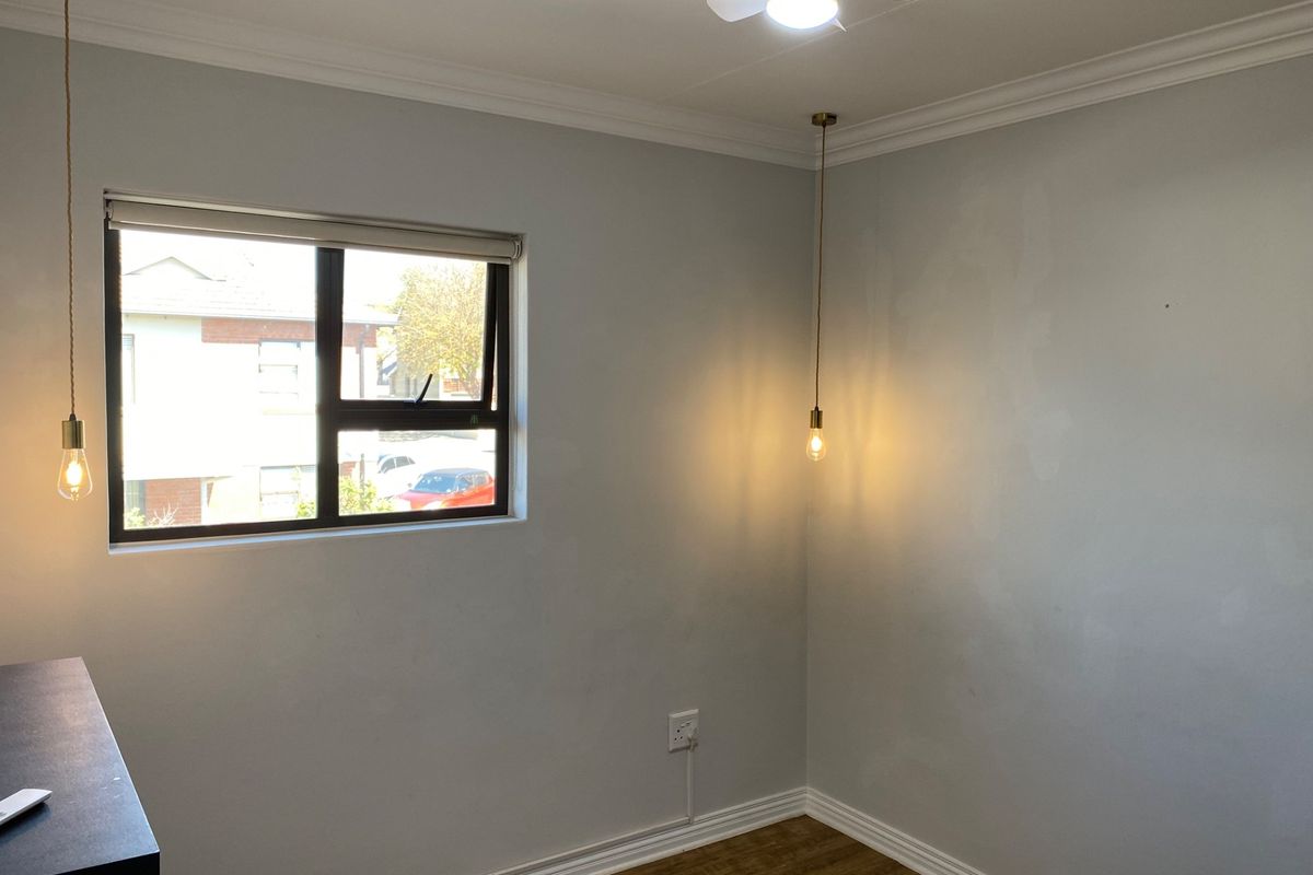 An empty bedroom featuring laminate flooring, modern pendant lighting, a ceiling fan, and neutral wall finishes.