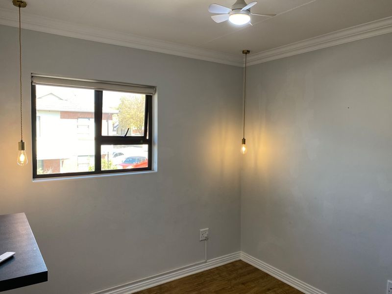 An empty bedroom featuring laminate flooring, modern pendant lighting, a ceiling fan, and neutral wall finishes.
