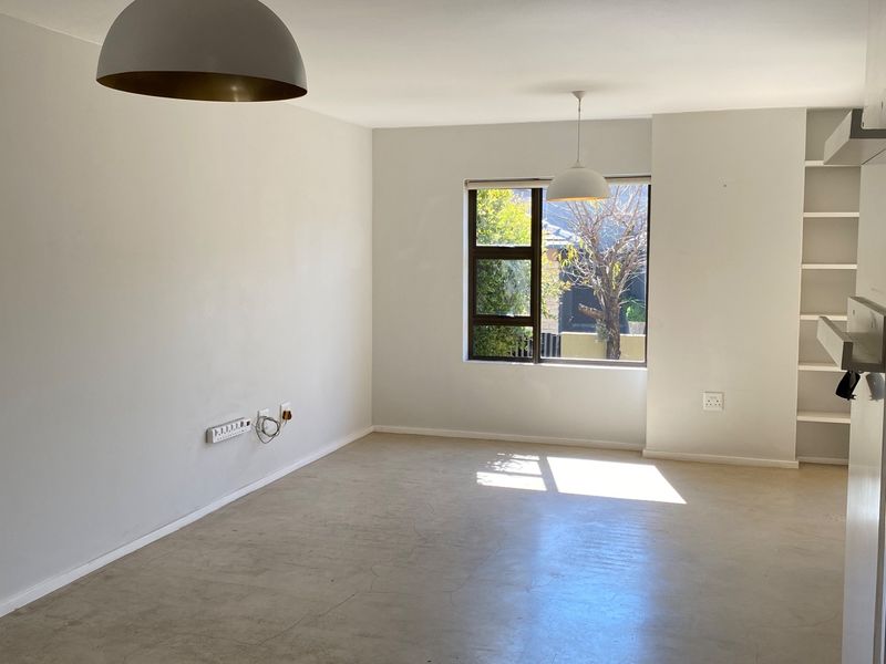 A bright, empty living room featuring polished concrete floors, built-in shelving, and modern pendant lighting, offering a clean canvas for interior design.