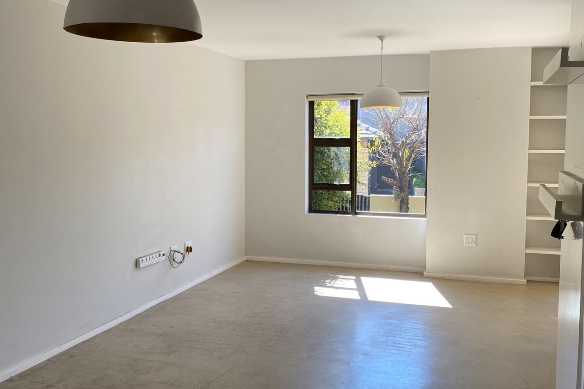 A bright, empty living room featuring polished concrete floors, built-in shelving, and modern pendant lighting, offering a clean canvas for interior design.