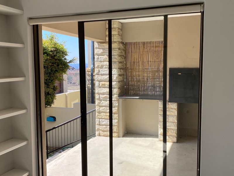 Covered patio area featuring a built-in braai, stone-clad pillar, and sliding glass door access, offering a functional outdoor entertainment space.