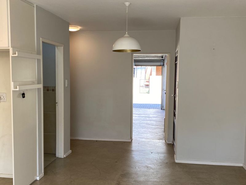 A neutral-toned hallway featuring concrete flooring and dual lighting fixtures, providing a clear transition space leading toward the exterior garage area.