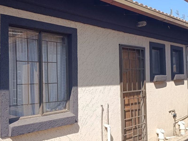 Rear exterior view of the property featuring textured plaster walls, security gates, and security bars on windows with a paved walkway.