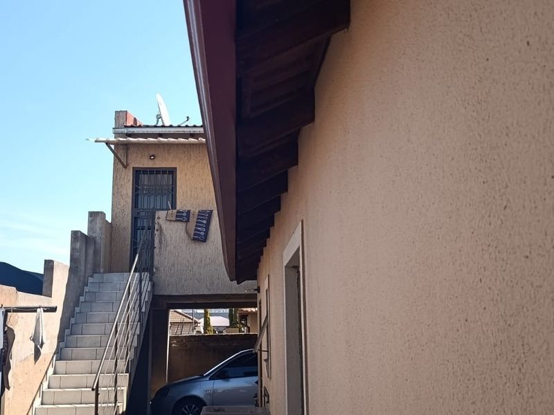 Rear exterior view of the property featuring an external staircase with tiled steps and metal railings leading to an upper level.