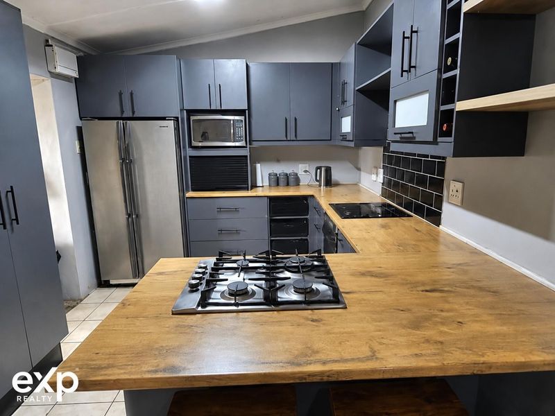 Modern kitchen featuring dark cabinetry, wooden countertops, a gas hob, integrated microwave, and a stylish black tiled backsplash.