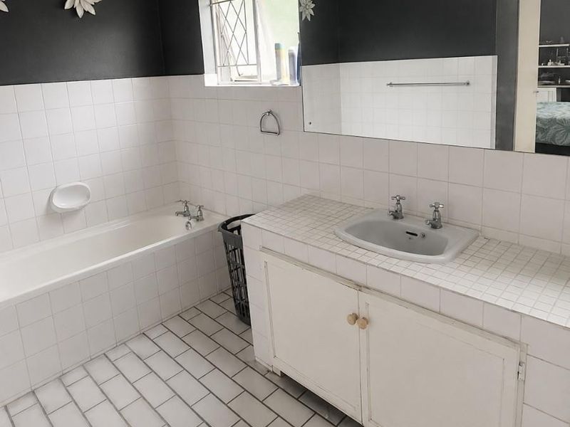 A functional bathroom featuring a built-in vanity with basin, a bathtub, and tiled finishes, offering a neutral base for potential modern updates.