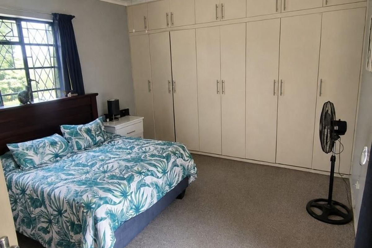 A bedroom featuring extensive built-in cupboards, a ceiling fan, and security bars on the window, finished with neutral carpeting.