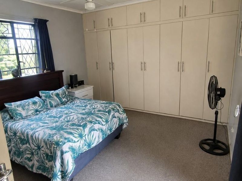 A bedroom featuring extensive built-in cupboards, a ceiling fan, and security bars on the window, finished with neutral carpeting.