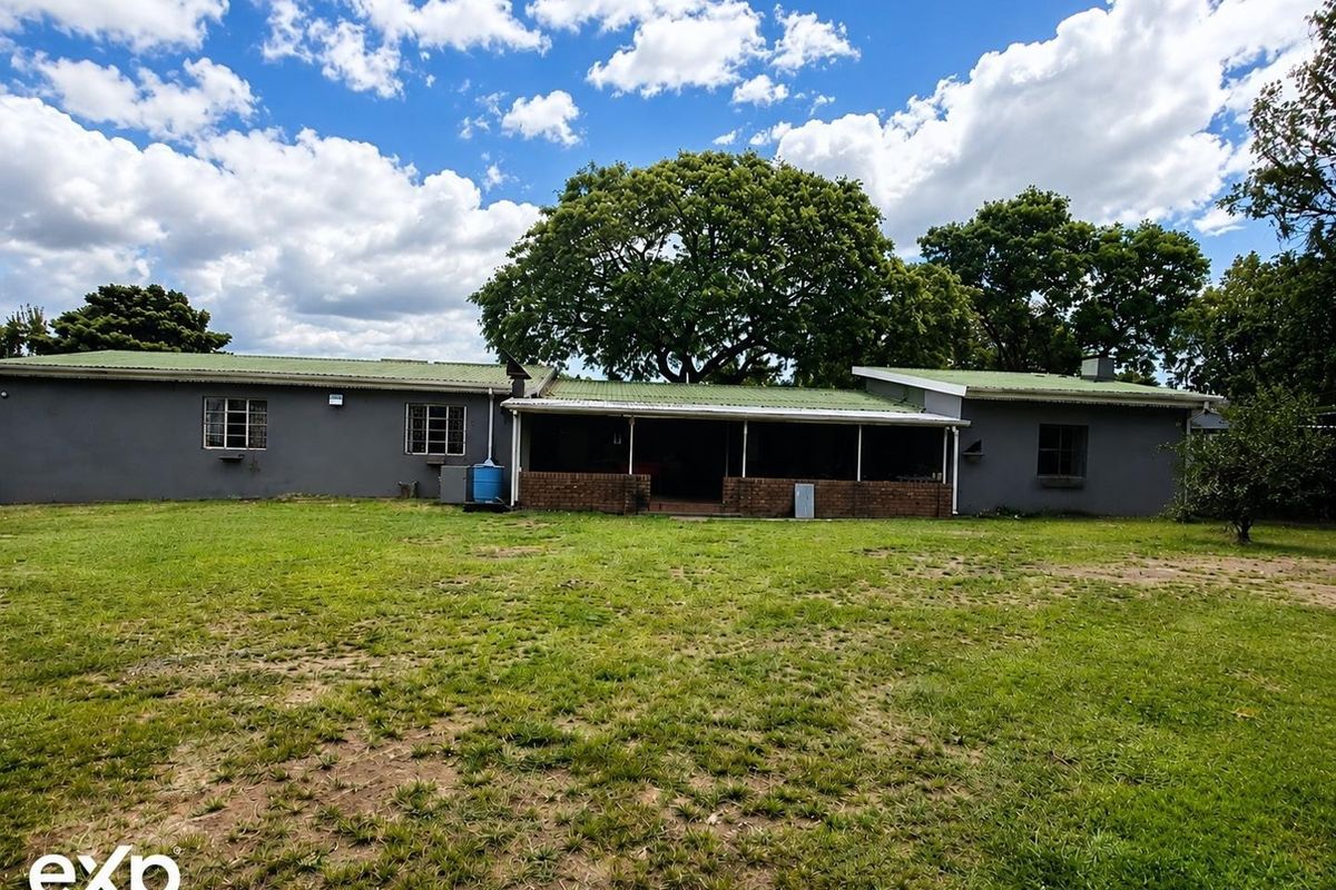 Rear view of the house featuring a covered patio area, corrugated metal roofing, and a large backyard with established trees.