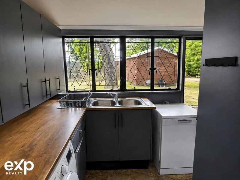 A functional scullery featuring dark cabinetry, a wooden countertop, double bowl sink, and leaded glass windows overlooking the rear garden.