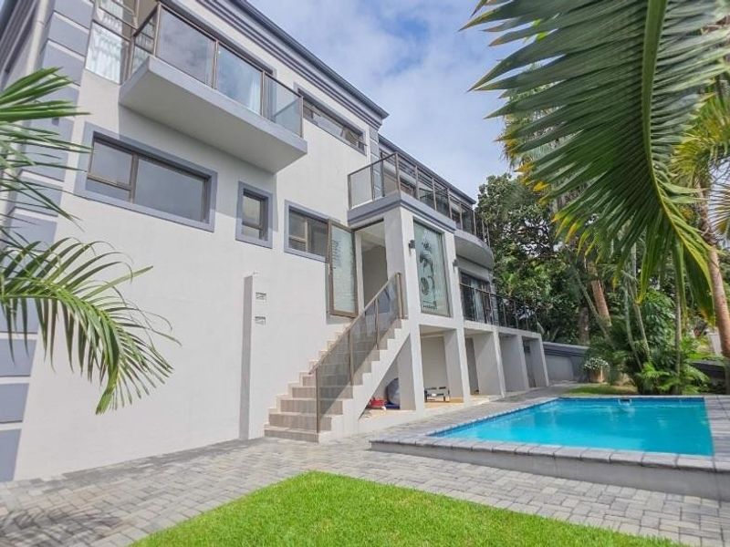 Rear view of a multi-story modern home featuring a swimming pool, paved patio area, and multiple balconies with glass balustrades.