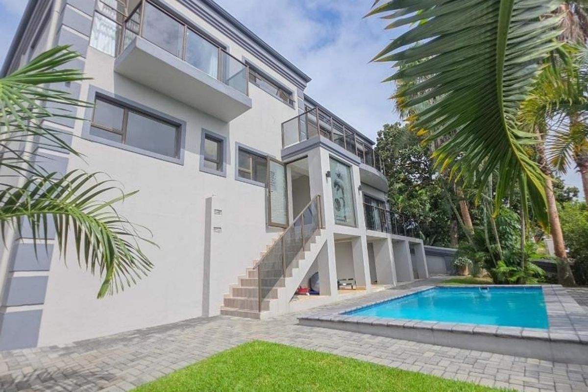 Rear view of a multi-story modern home featuring a swimming pool, paved patio area, and multiple balconies with glass balustrades.