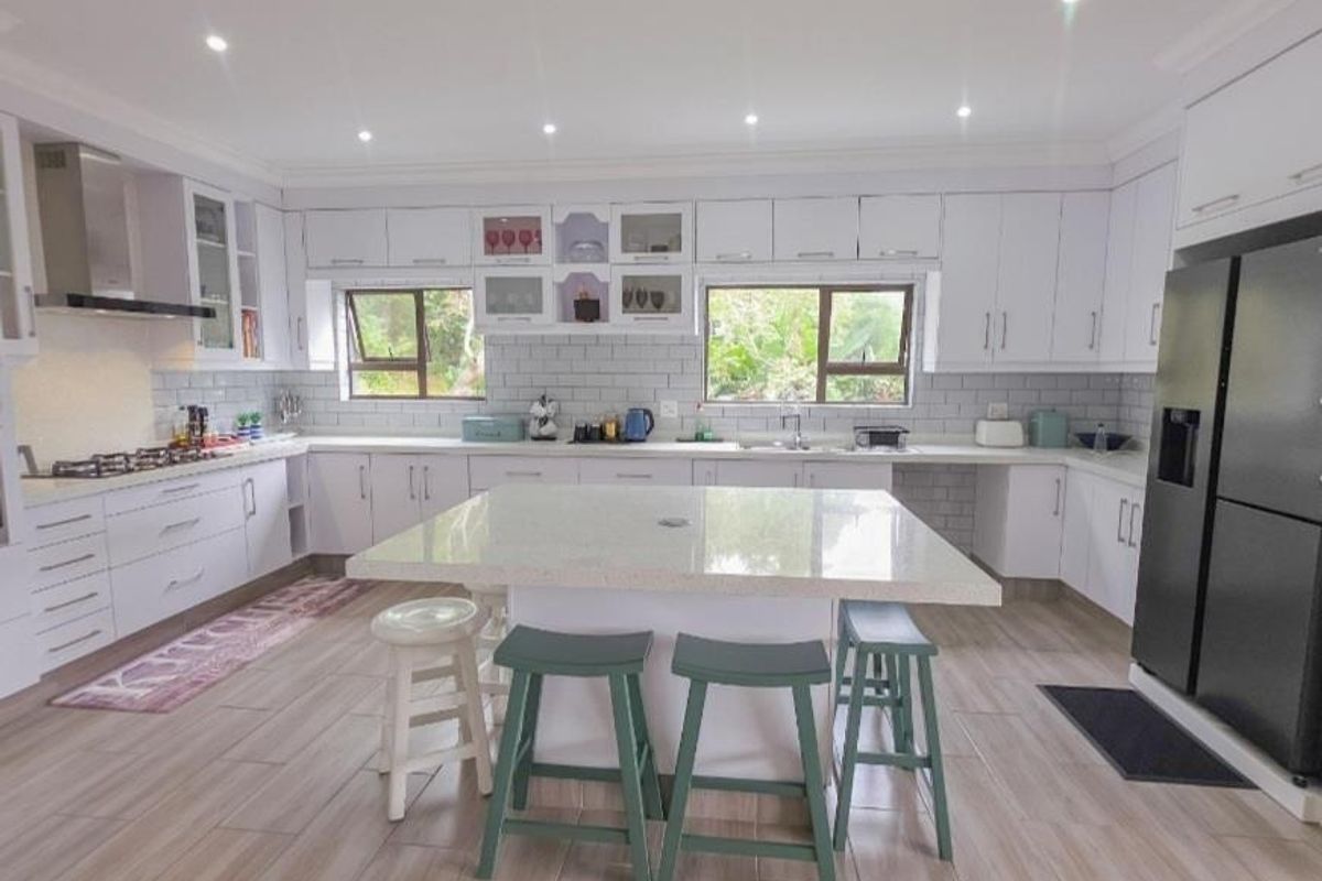Modern, well-lit kitchen featuring white cabinetry, stone countertops, a central island, subway tile backsplash, and high-quality built-in appliances.