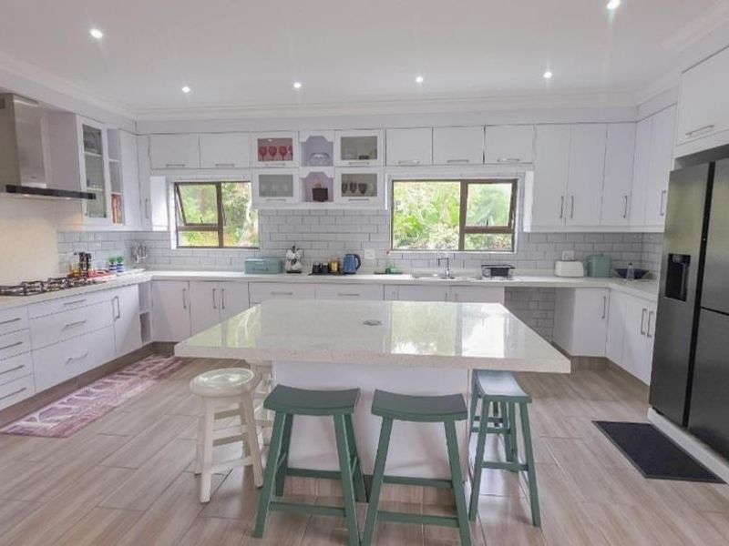 Modern, well-lit kitchen featuring white cabinetry, stone countertops, a central island, subway tile backsplash, and high-quality built-in appliances.