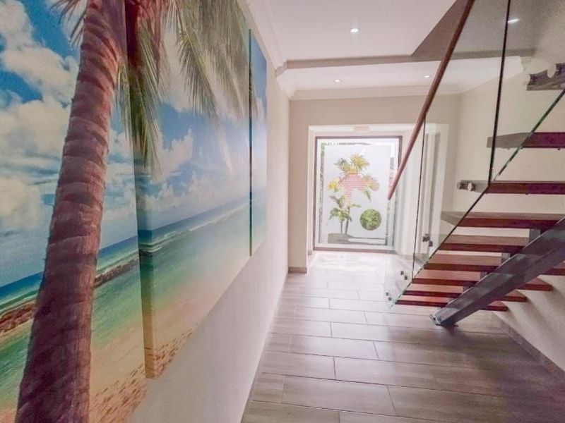 Modern hallway featuring a floating staircase with glass balustrade, tiled flooring, and recessed ceiling lighting leading to a bright rear entrance.