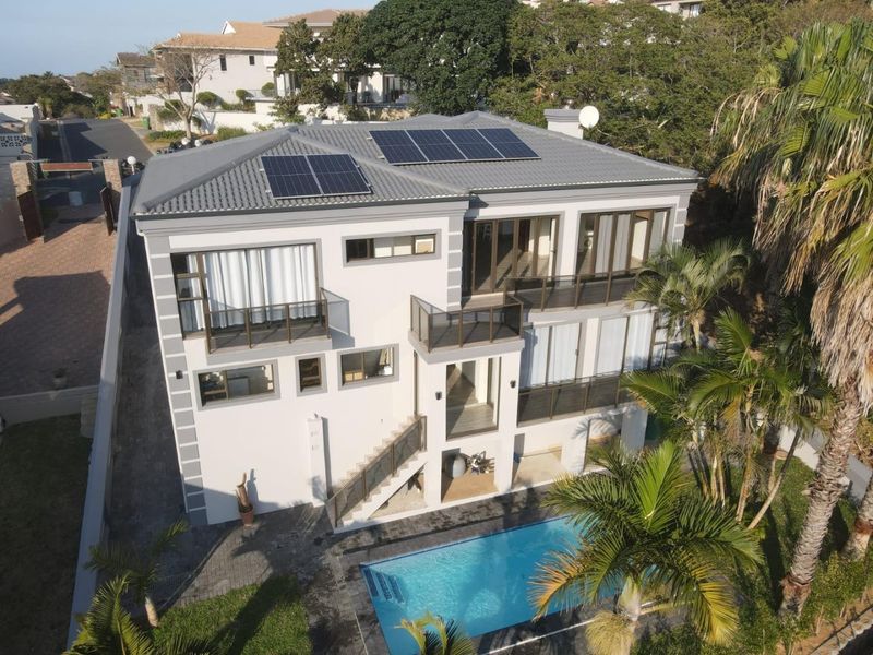 Aerial view of a modern multi-story house featuring a tiled roof with solar panels, multiple balconies, an external staircase, and a private swimming pool.